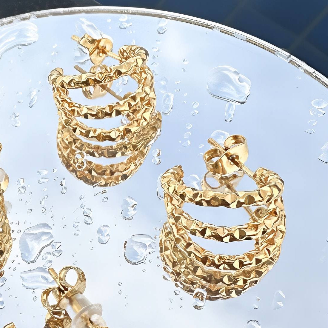 Gold hammered triple hoop earrings on a textured surface with water droplets