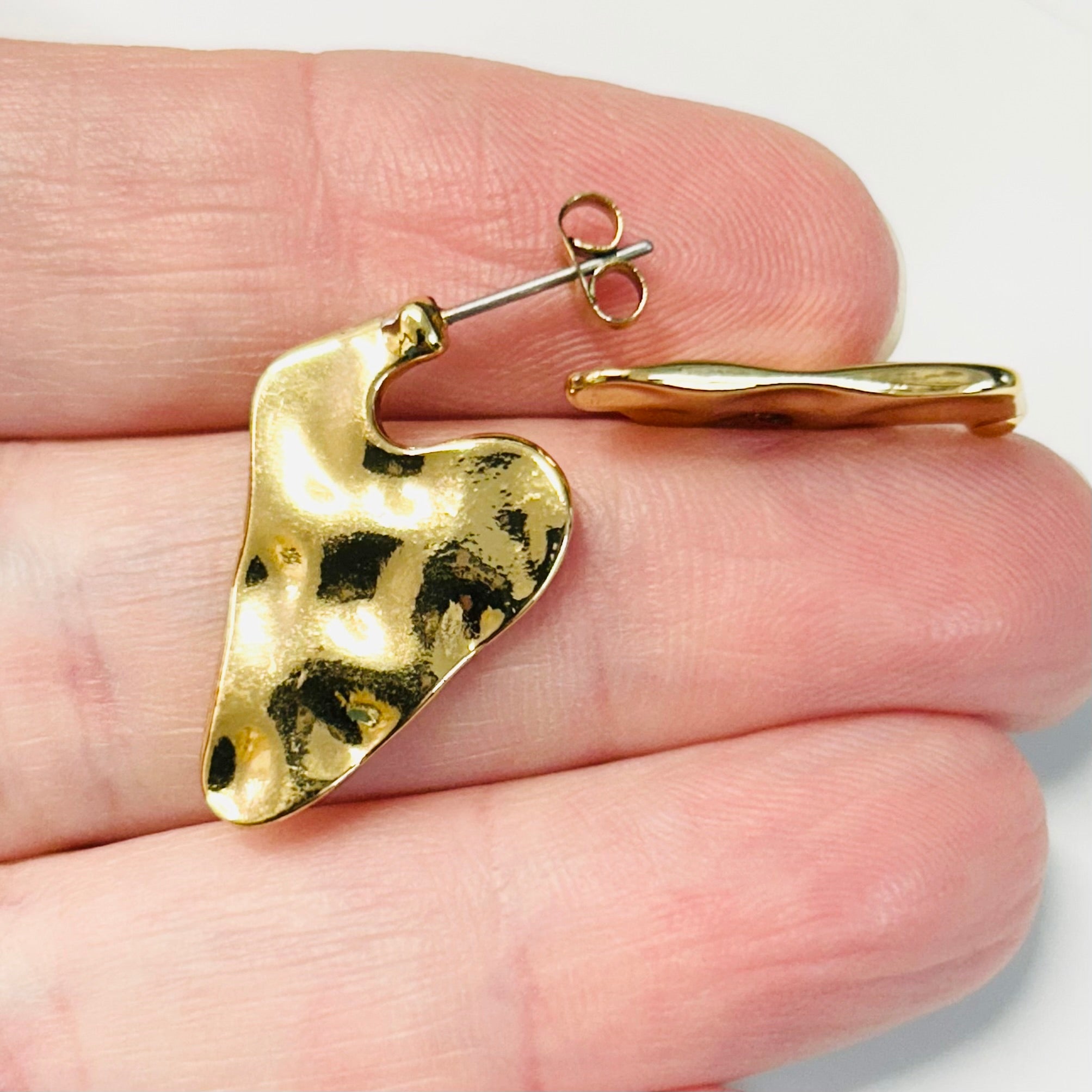 Gold heart-shaped earring on a hand with a white background