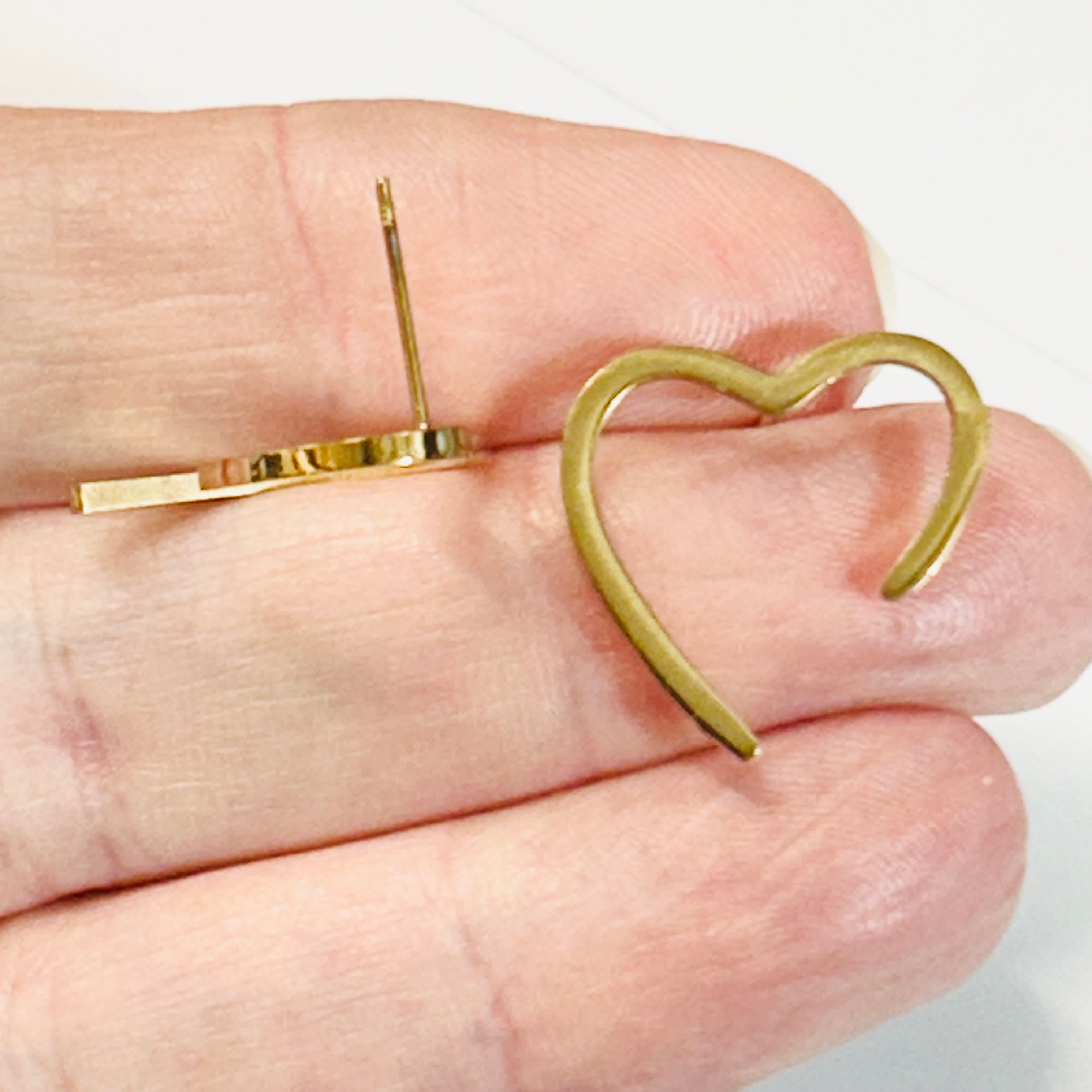Gold heart-shaped earring held between fingers on a light background