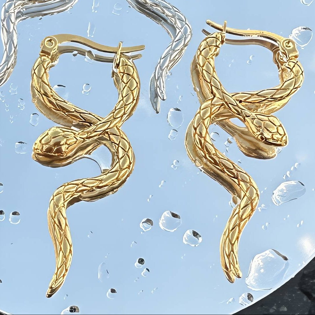 Gold snake-shaped earrings on a textured blue surface.