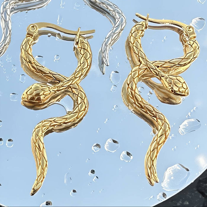 Gold snake-shaped earrings on a textured blue surface.