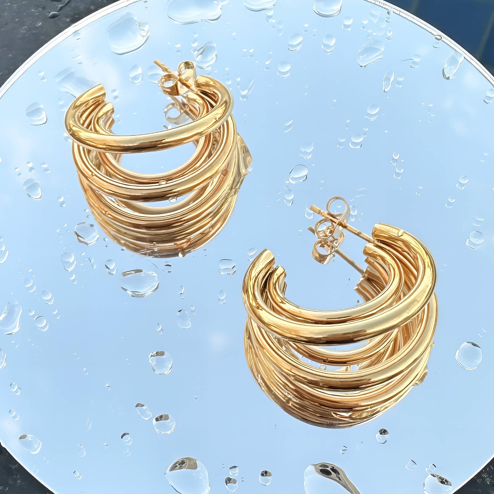 Gold hoop earrings on a clear glass surface with water droplets.