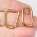 Gold hoop earrings held between fingers against a neutral background