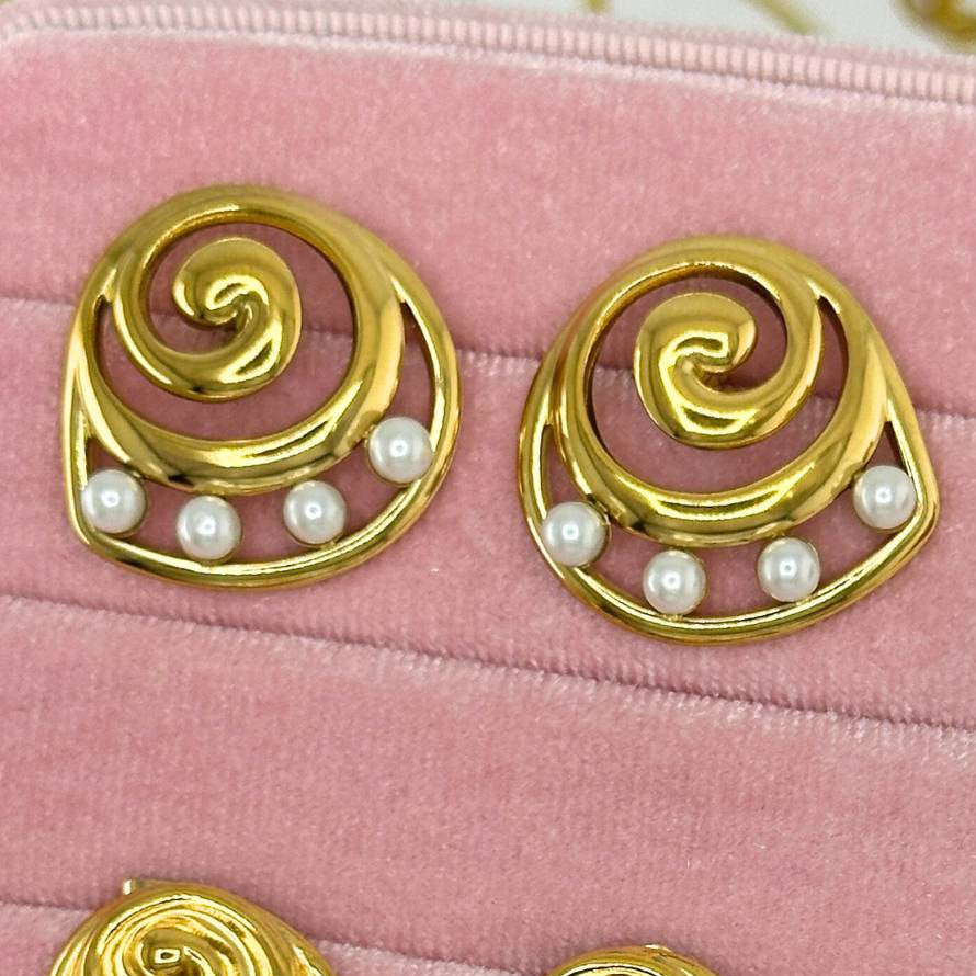 Set of gold earrings with pearls and gemstones on a pink velvet surface