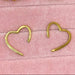 Gold heart-shaped earrings on a pink textured background