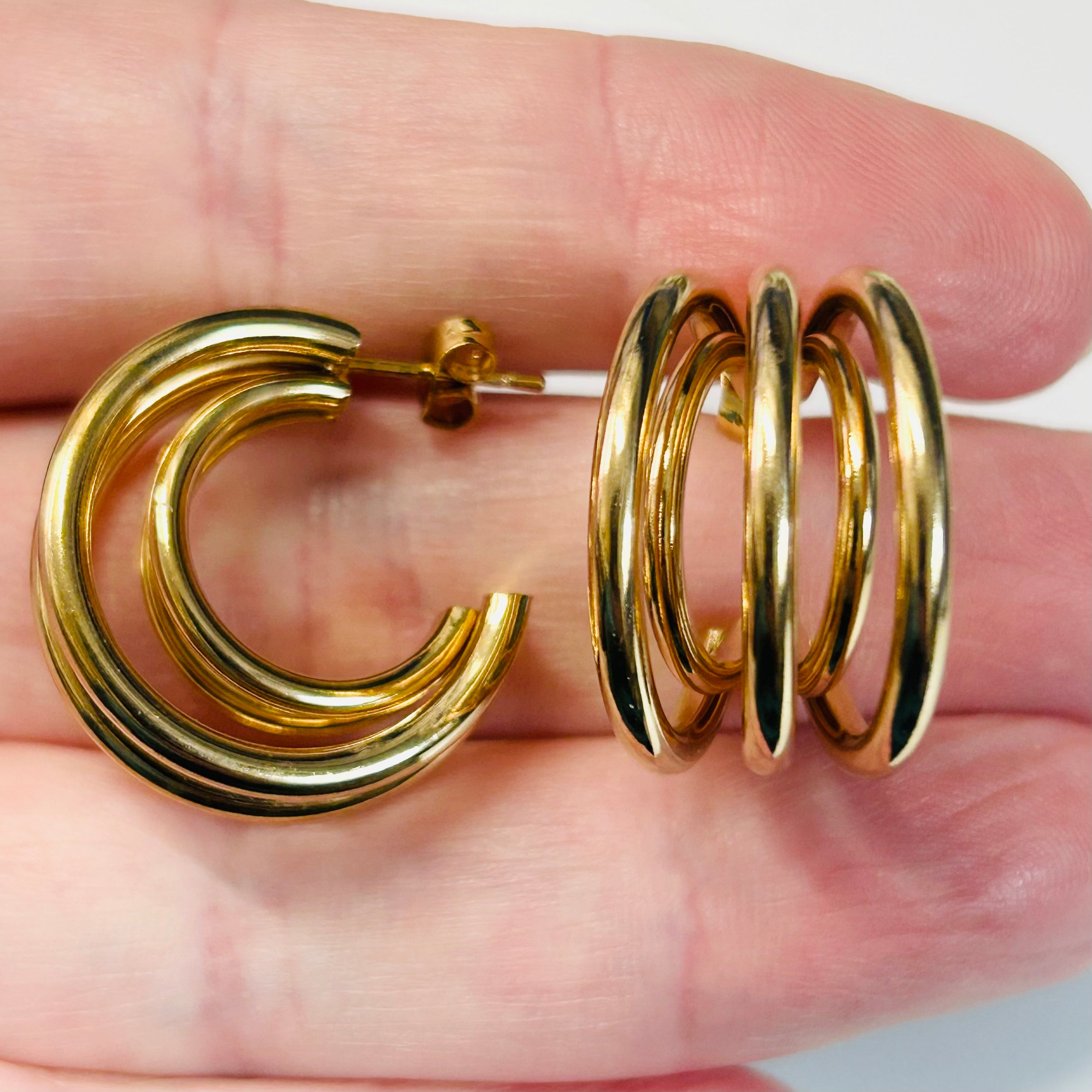 Gold hoop earrings held between fingers against a neutral background