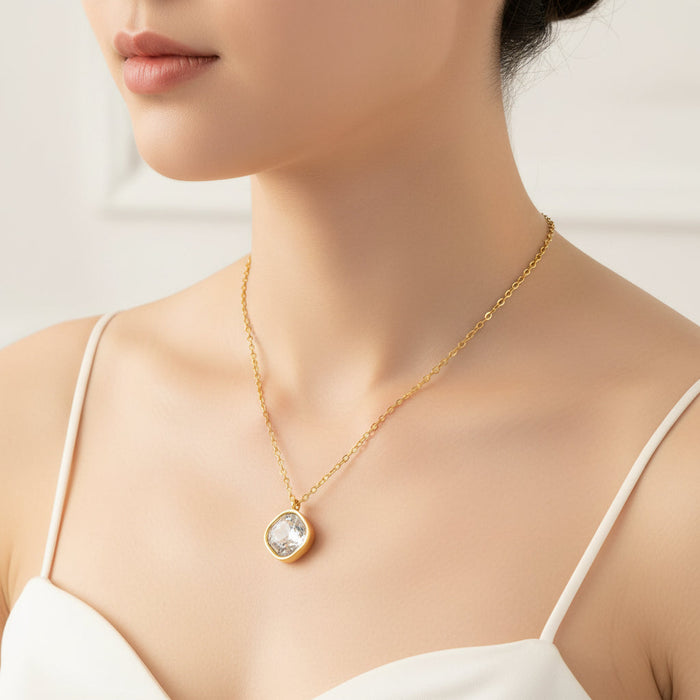 Gold necklace with a pendant on a model wearing a white top against a neutral background