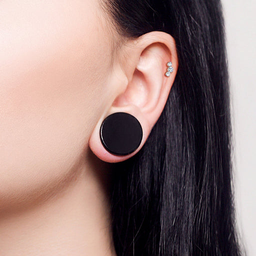 Close-up of an ear wearing black round earrings with a neutral background