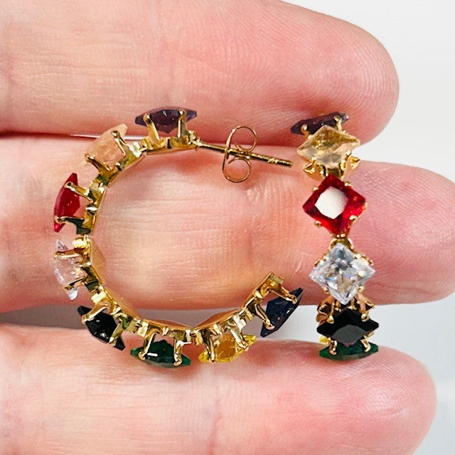 Colorful gemstone hoop earrings held between fingers against a neutral background